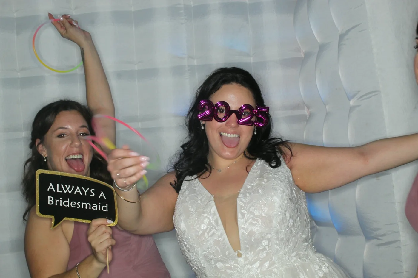 Bride and bridesmaid in front of a white photo booth backdrop